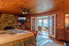 Relax in a warm and inviting space with a large bed, stone fireplace, and ceiling fan.