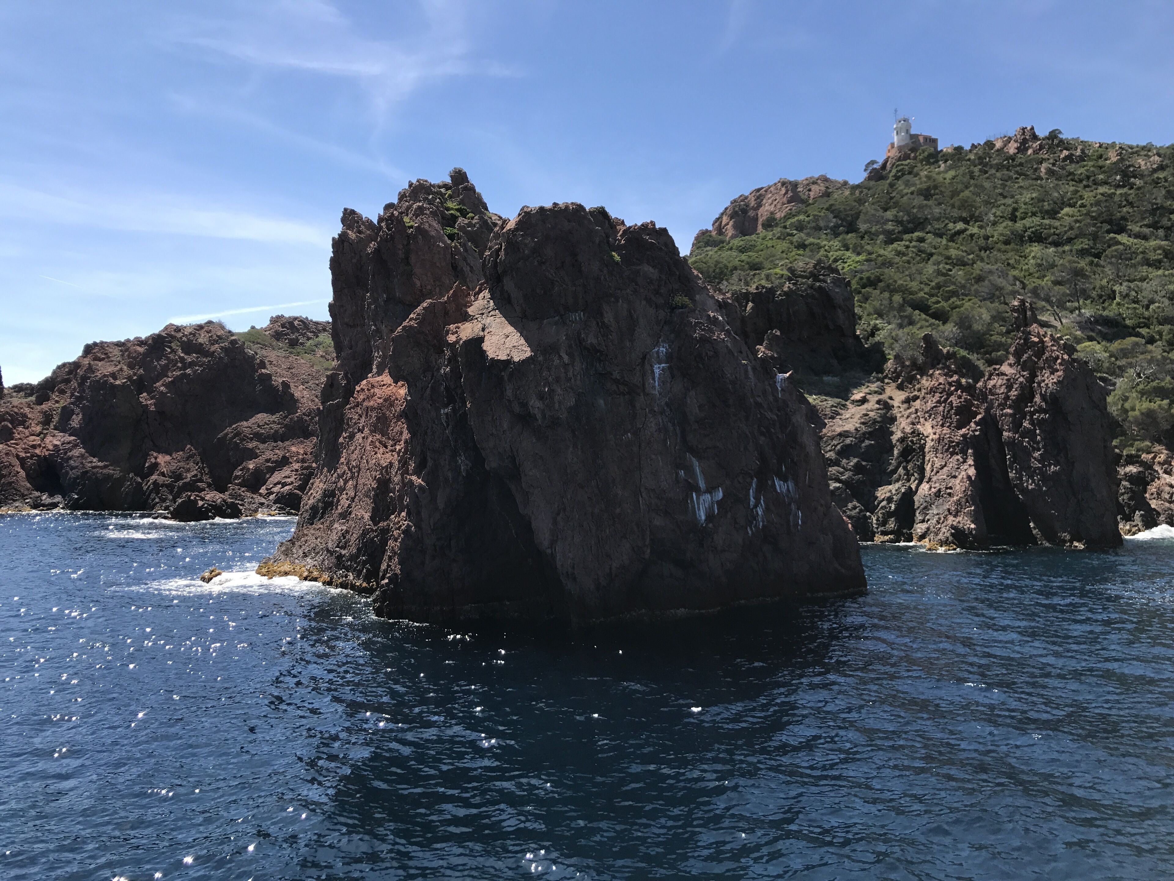 Un paisaje costero rocoso con una formación rocosa destacada en primer plano y una colina con vegetación escasa al fondo.