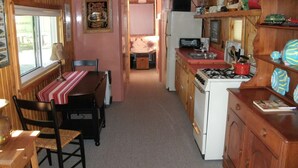 A compact kitchen with wooden cabinets, a dining table with chairs, and a small island with a stove. - Cozy, Quiet, Getaway for Single or Couple (Big Bay)