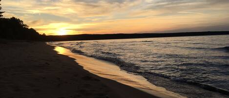 A beach with a sunset, calm water, and a distant shoreline.