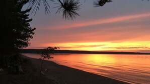 A beach with a sunset over the water, trees, and a distant shoreline. - Cozy, Quiet, Getaway for Single or Couple (Big Bay)