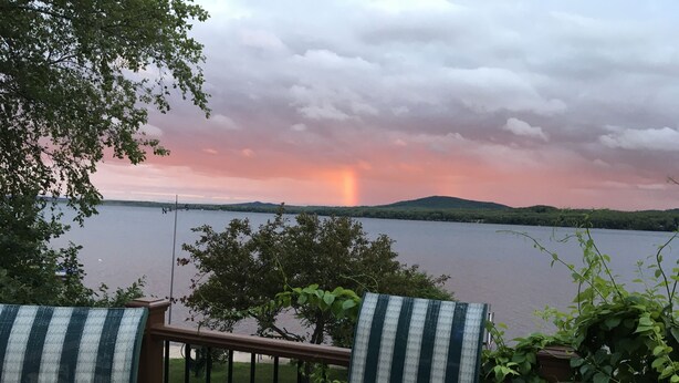 A glass table and chairs on a balcony overlooking a lake with a sunset. - Cozy, Quiet, Getaway for Single or Couple (Big Bay)