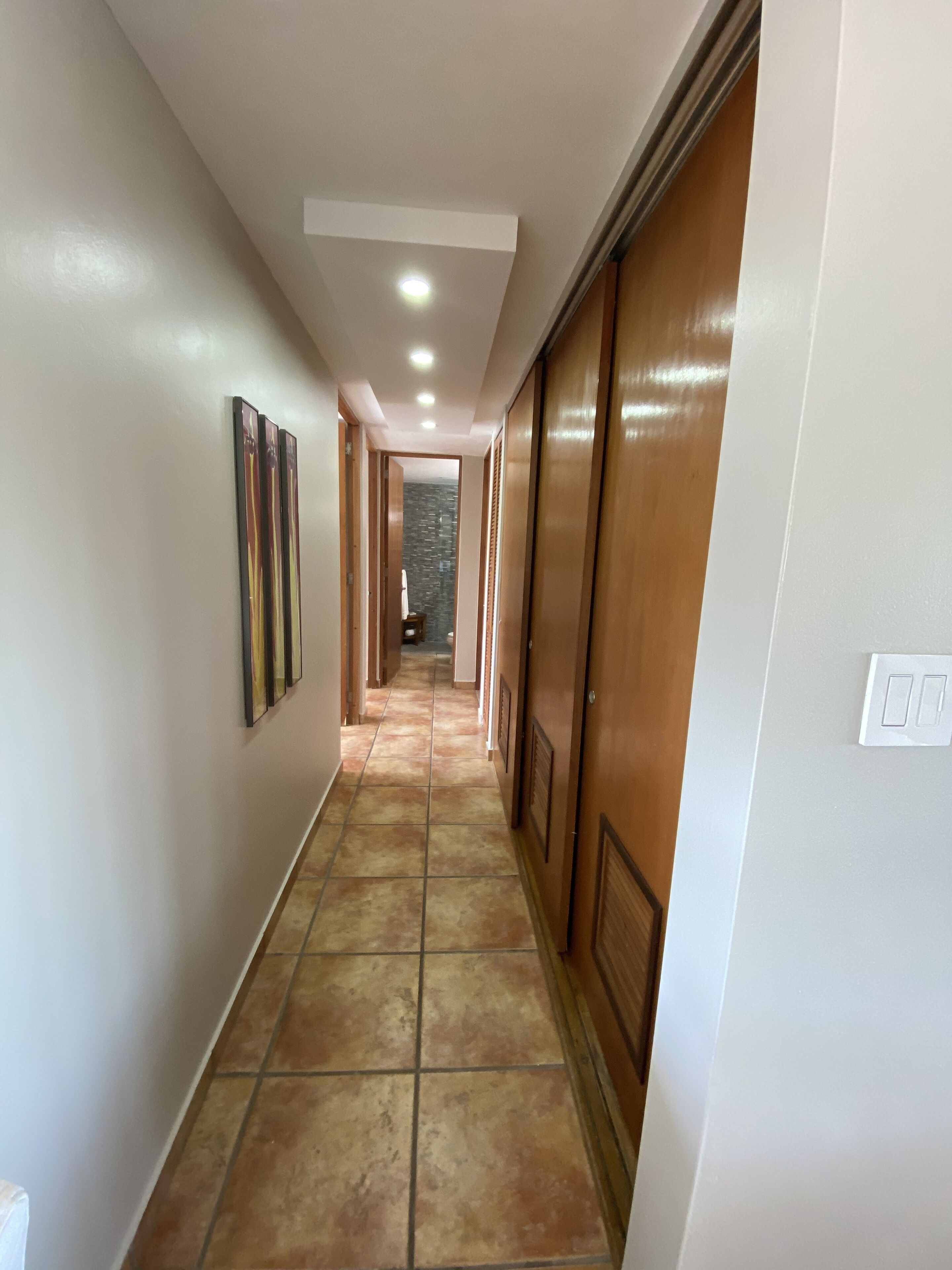 A hallway with tiled flooring, wooden doors, and a tiled wall.