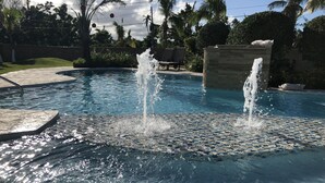 A clear pool with two water jets, surrounded by a stone wall and palm trees. - BEACHFRONT > 5 STAR > 2 LEVEL PENTHOUSE VILLA > MAGNIFICENT PANORAMIC VIEWS  (Barrio Las Cabezas, Fajardo)