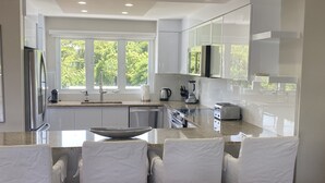 A modern kitchen with a central island, stainless steel appliances, and a view of greenery outside. - BEACHFRONT > 5 STAR > 2 LEVEL PENTHOUSE VILLA > MAGNIFICENT PANORAMIC VIEWS  (Barrio Las Cabezas, Fajardo)