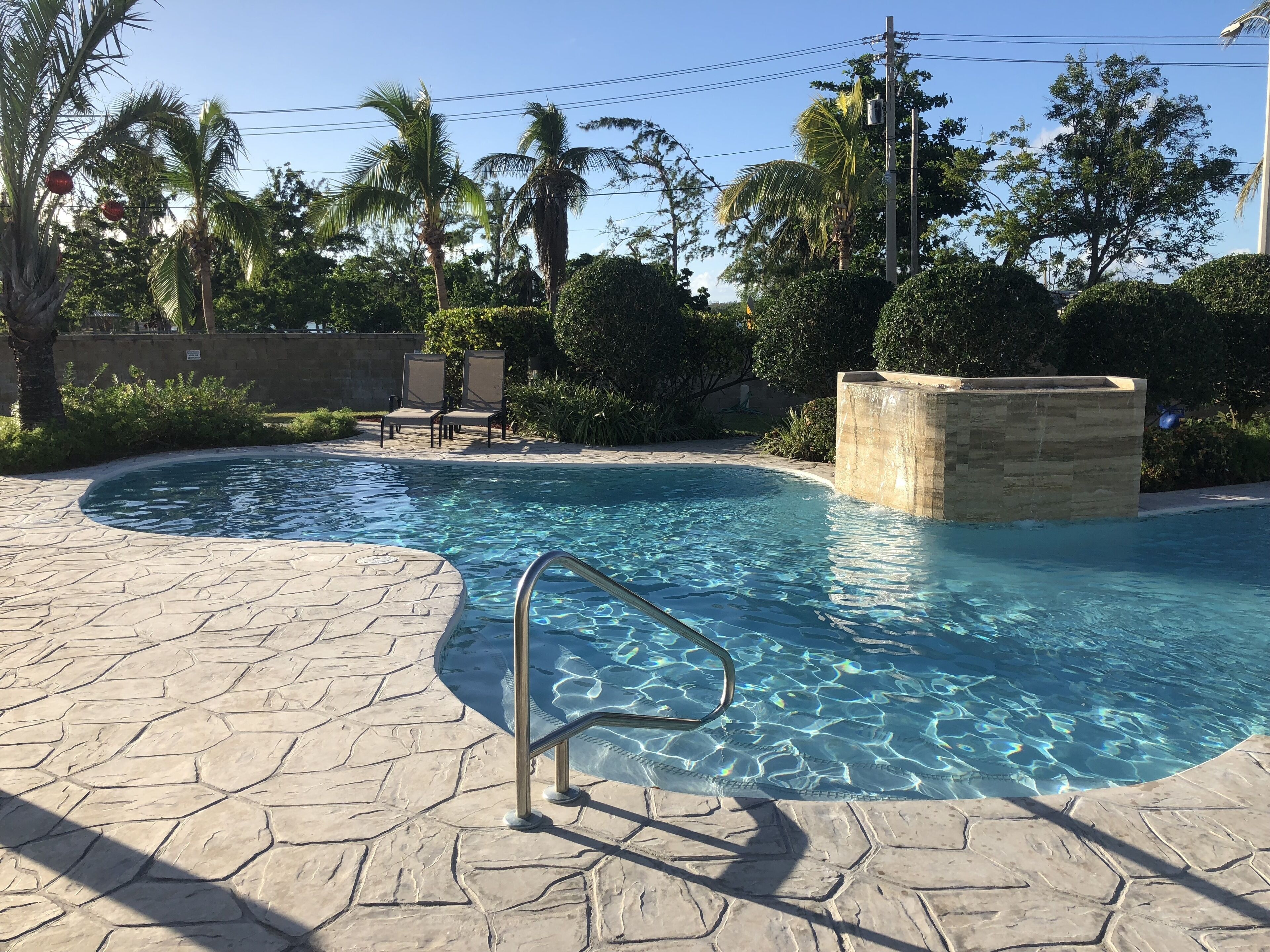 A swimming pool with a stone deck, a metal ladder, and lounge chairs.