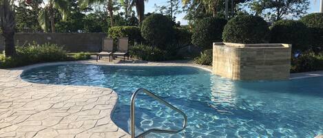 A swimming pool with a stone deck, a metal ladder, and lounge chairs.