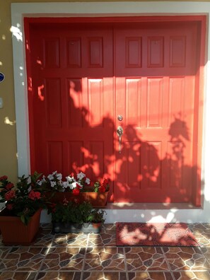 A red door with a keyhole and a doormat in front. There are potted plants to the left of the door. - Modern & Spacious Townhouse near Beaches, Airport, Grocery Stores & Resataurants (Nassau)