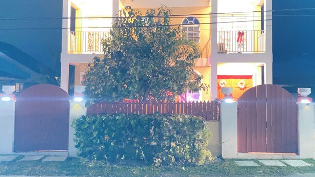 A two-story house with a balcony, a gated entrance, and a well-lit front yard.