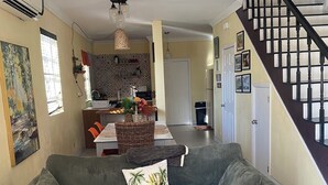 A living room with a green sofa, a dining area with a kitchen in the background, and a staircase to the right.