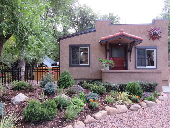 A two-story house with a red door, a small porch, and a garden with various plants and rocks.