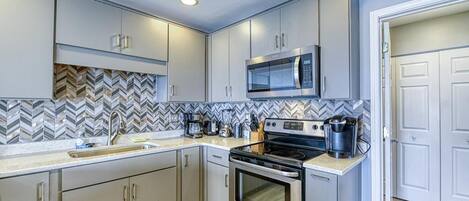 A modern kitchen with stainless steel appliances, a herringbone tile backsplash, and light-colored cabinetry.