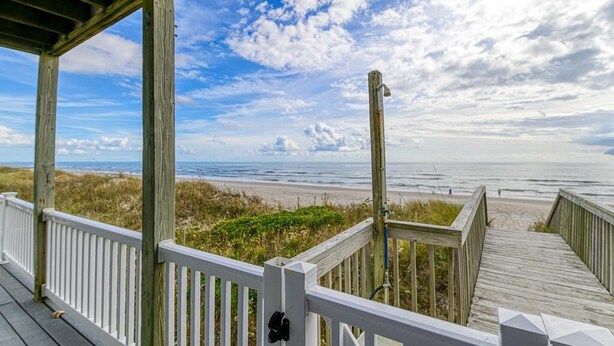 Een houten terras met witte leuningen met uitzicht op een strand.