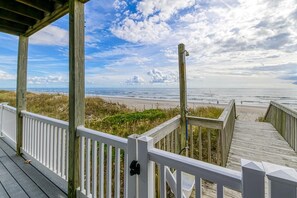 A wooden deck with white railings overlooking a beach.