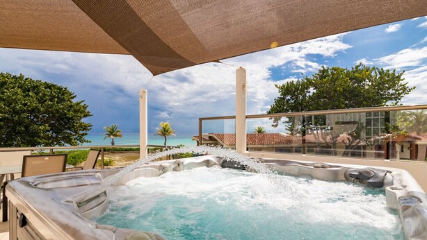Ein Whirlpool mit Meerblick, umgeben von Gartenmöbeln und einer überdachten Sitzgelegenheit.