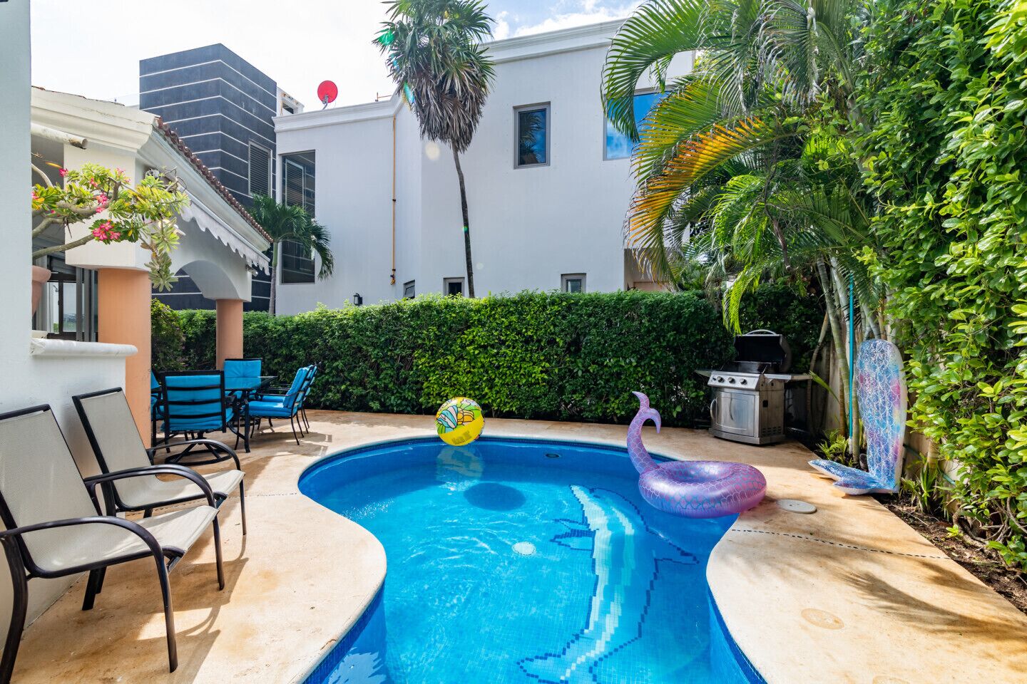 Patio trasero con piscina, flotador tiki y mobiliario exterior.