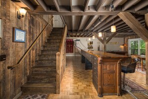 A rustic interior with a wooden staircase, a long bar area, and a herringbone-patterned floor. - Historic Beech Mountain Lodge | Hot Tub | Game Room | Sleeps 19 (Beech Mountain)
