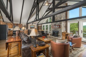 A spacious living area with a stone fireplace, leather seating, and a view of the outdoors. - Historic Beech Mountain Lodge | Hot Tub | Game Room | Sleeps 19 (Beech Mountain)