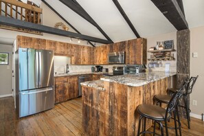 A kitchen with wooden cabinets, stainless steel appliances, a granite countertop, and a bar area with stools. - Historic Beech Mountain Lodge | Hot Tub | Game Room | Sleeps 19 (Beech Mountain)