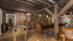 A rustic room with a wooden foosball table, a bar area with stools, and a staircase. - Historic Beech Mountain Lodge | Hot Tub | Game Room | Sleeps 19 (Beech Mountain)