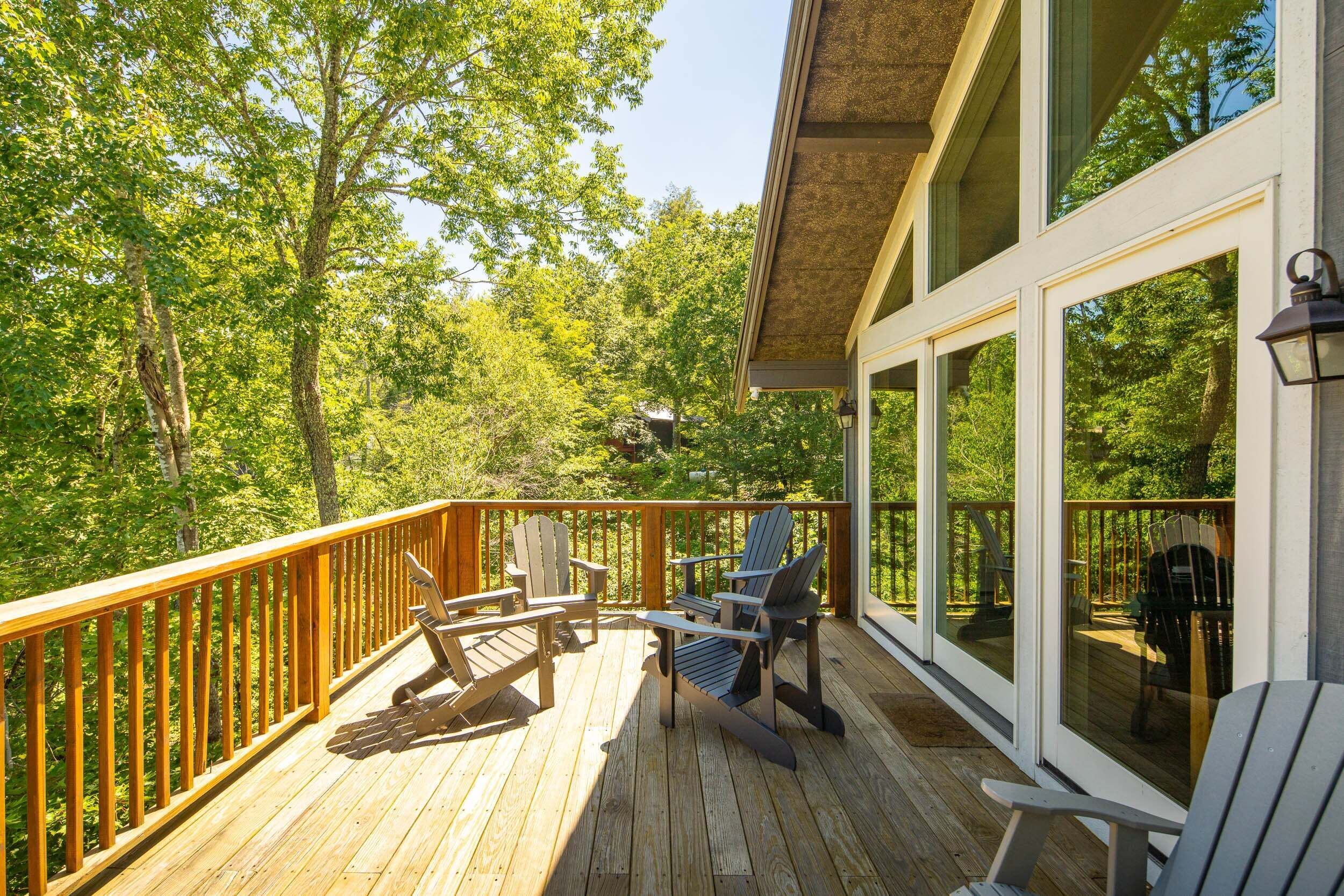 A wooden deck with Adirondack chairs and a table, overlooking a forested area.