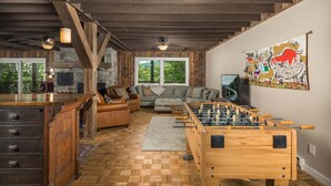 A rustic interior with a wooden ceiling, a sofa, a leather armchair, a foosball table, and a stone wall with a painting. - Historic Beech Mountain Lodge | Hot Tub | Game Room | Sleeps 19 (Beech Mountain)