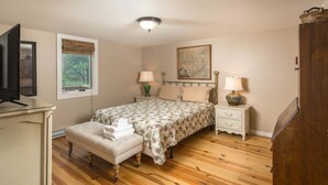 A bedroom with a bed, two bedside tables with lamps, a wooden floor, a window with a view, and a television on a stand. - Historic Beech Mountain Lodge | Hot Tub | Game Room | Sleeps 19 (Beech Mountain)