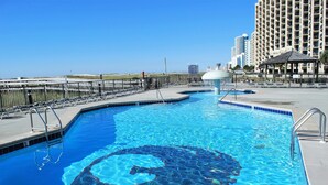 A swimming pool with a clear blue water feature, surrounded by a fence, and a tall building in the background. - Fun in the Sun! 3 bdrm/2 Bath Ocean Front Condo with gorgeous views of the Gulf! (Orange Beach)