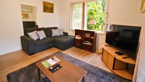 A living room with a sectional sofa, a TV, a wooden coffee table, and a bookshelf. - Snowy Mtn Lake Cottage | Pets & Groups | Sleeps 8 (Talbingo)