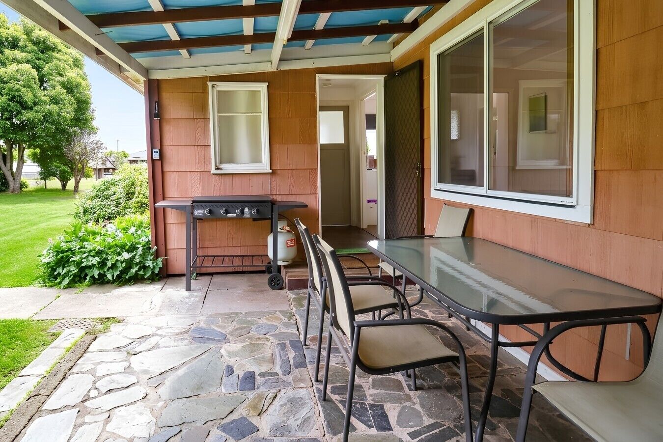An outdoor patio with a grill, a glass table, and chairs.