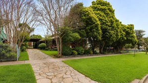 A stone pathway leading to a house with a well-maintained lawn and trees. - Snowy Mtn Lake Cottage | Pets & Groups | Sleeps 8 (Talbingo)