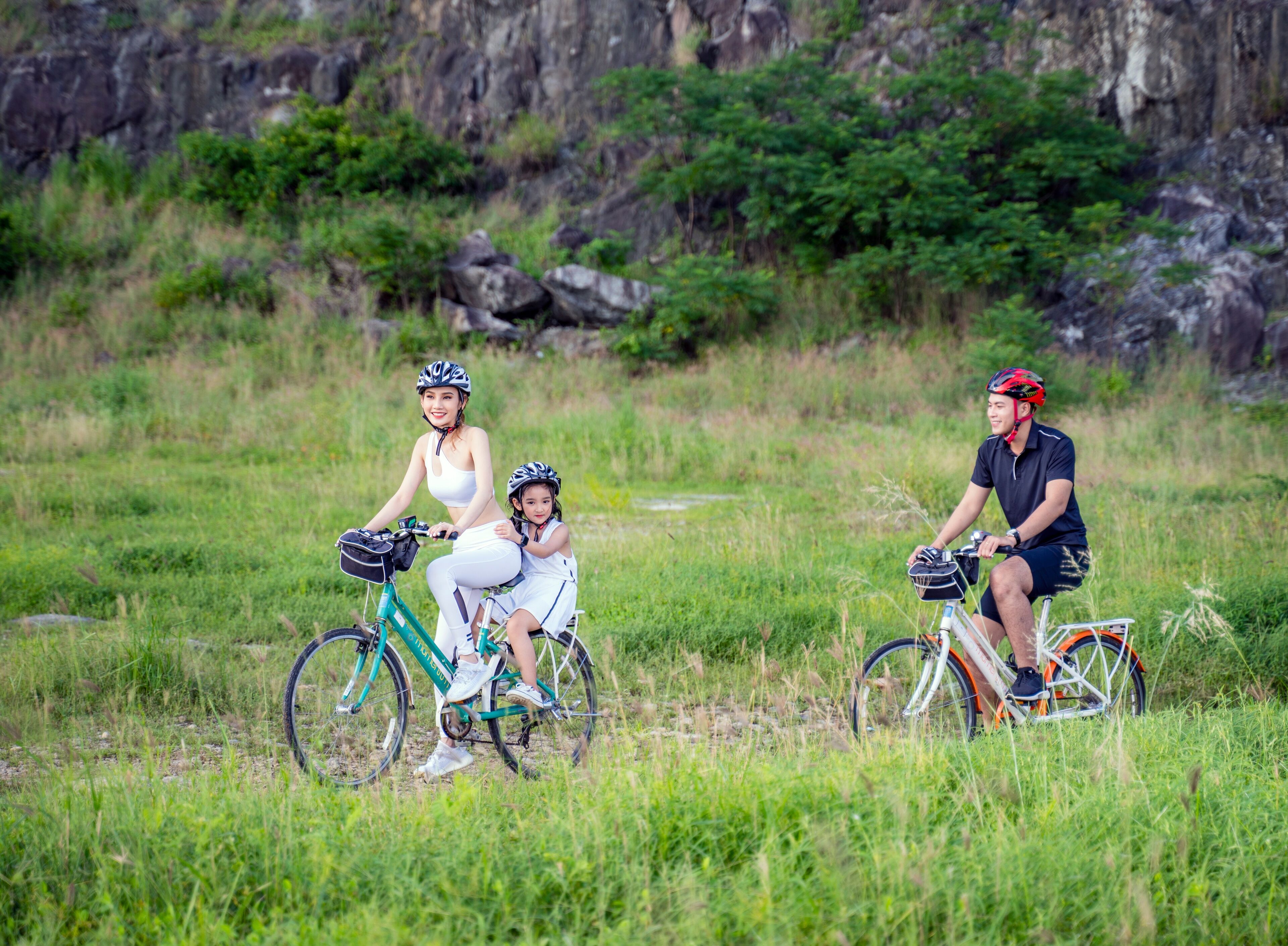 Three people on bicycles in a grassy field with rocky terrain in the background.