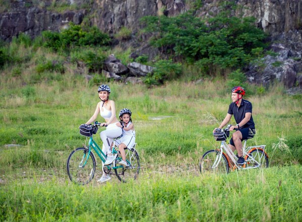 Tres personas en bicicletas sobre un campo cubierto de hierba, con terreno rocoso al fondo.