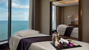 A hotel room with a large window offering a view of the sea, a bed with a dark brown bedspread, a tray with toiletries, and a mirror reflecting the room. - Four Points by Sheraton Danang (Da Nang)