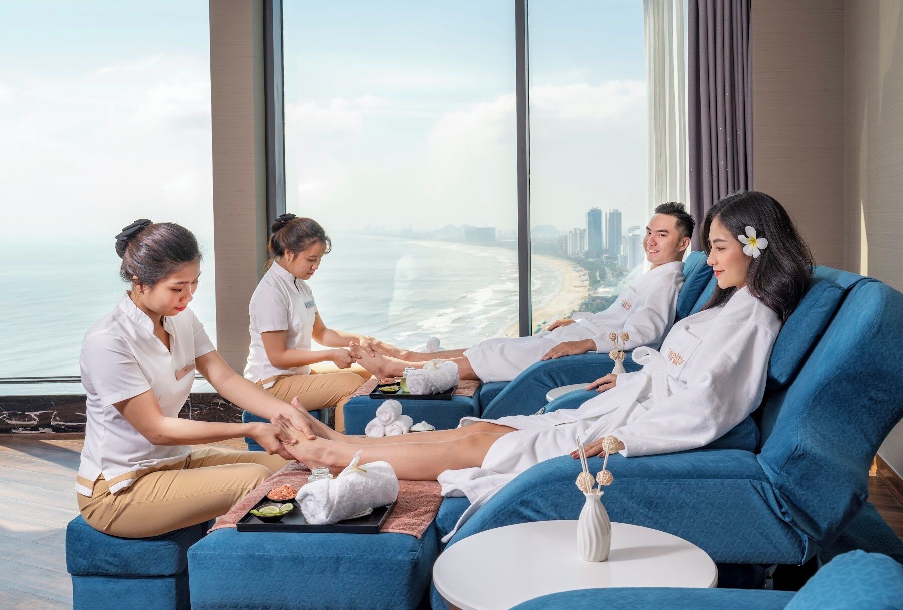 A group of people receiving a massage in a modern room with a large window overlooking a beach and cityscape.