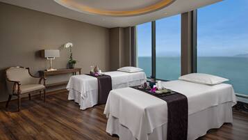 A hotel room with two beds, a chair, a nightstand, and a large window with a view of the sea.