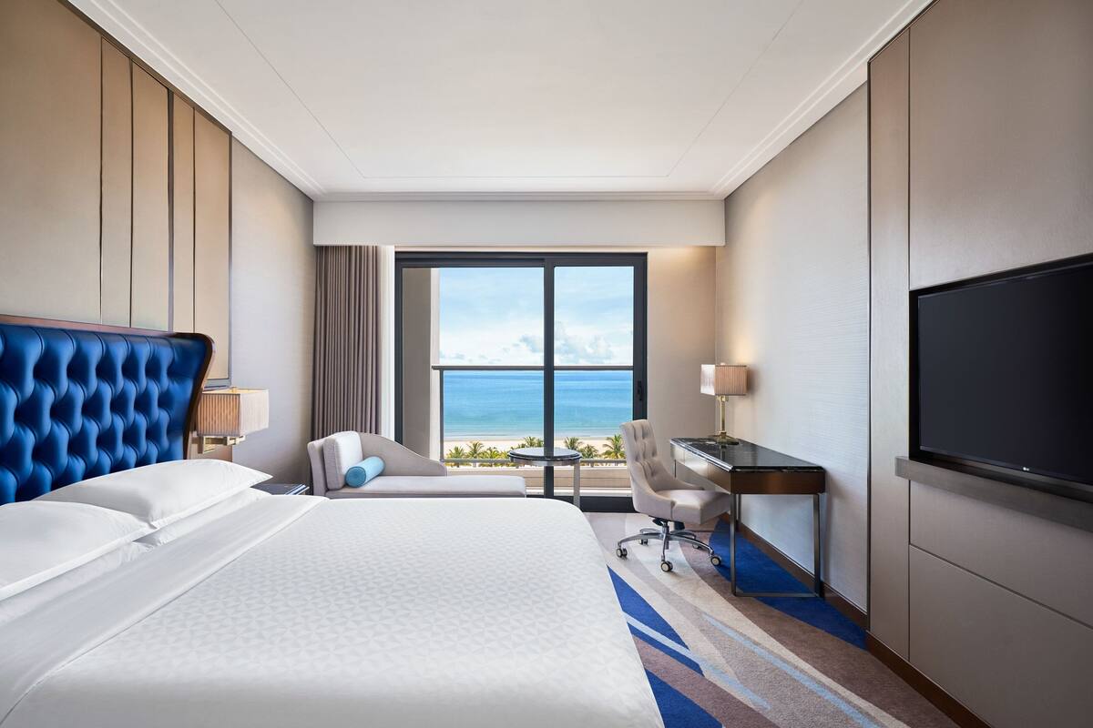 A hotel room with a large bed, a desk, a chair, and a TV.