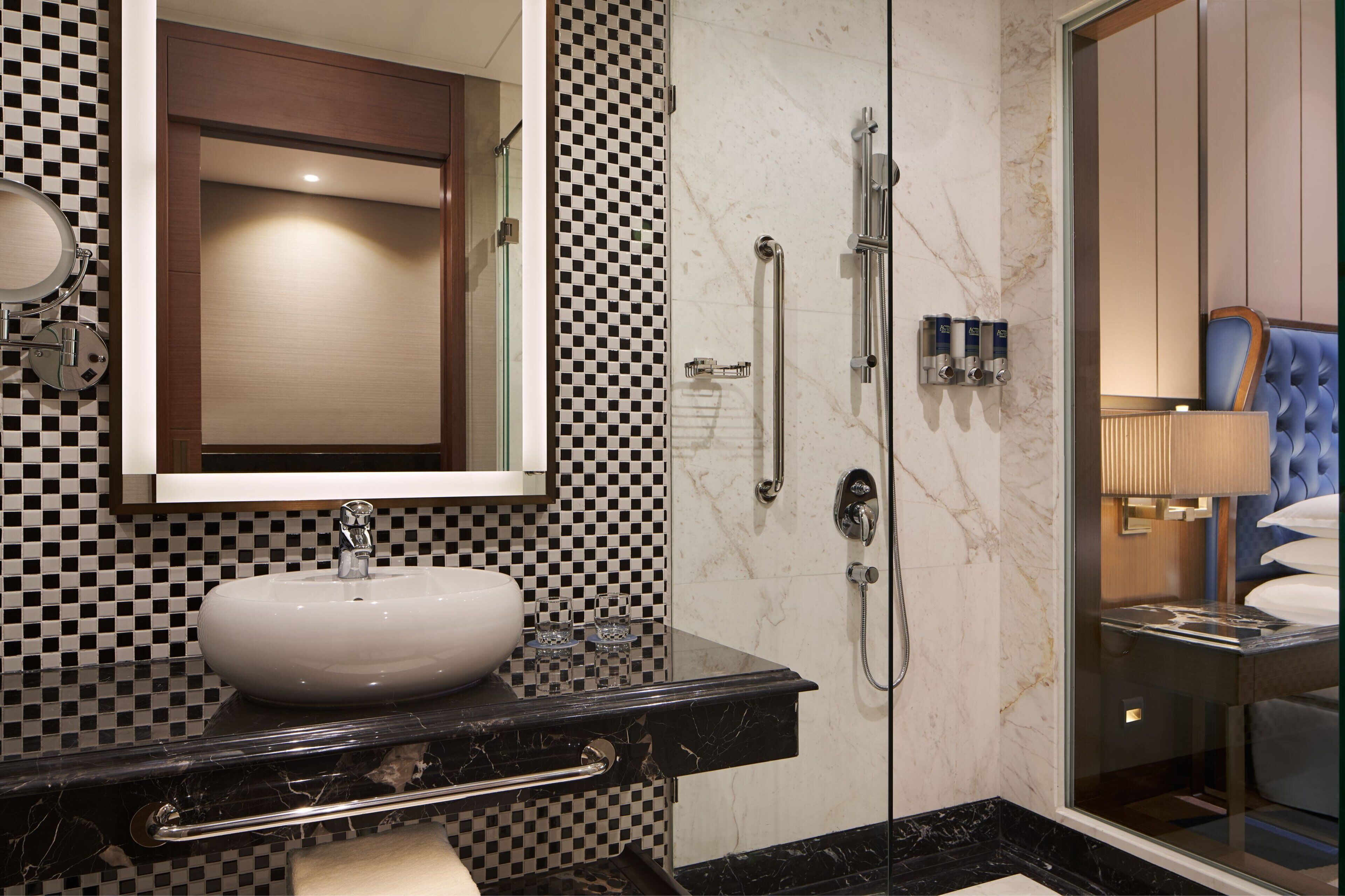 Un baño con un lavabo de mármol negro, un espejo, un pared con diseño de cuadros y una zona de ducha.