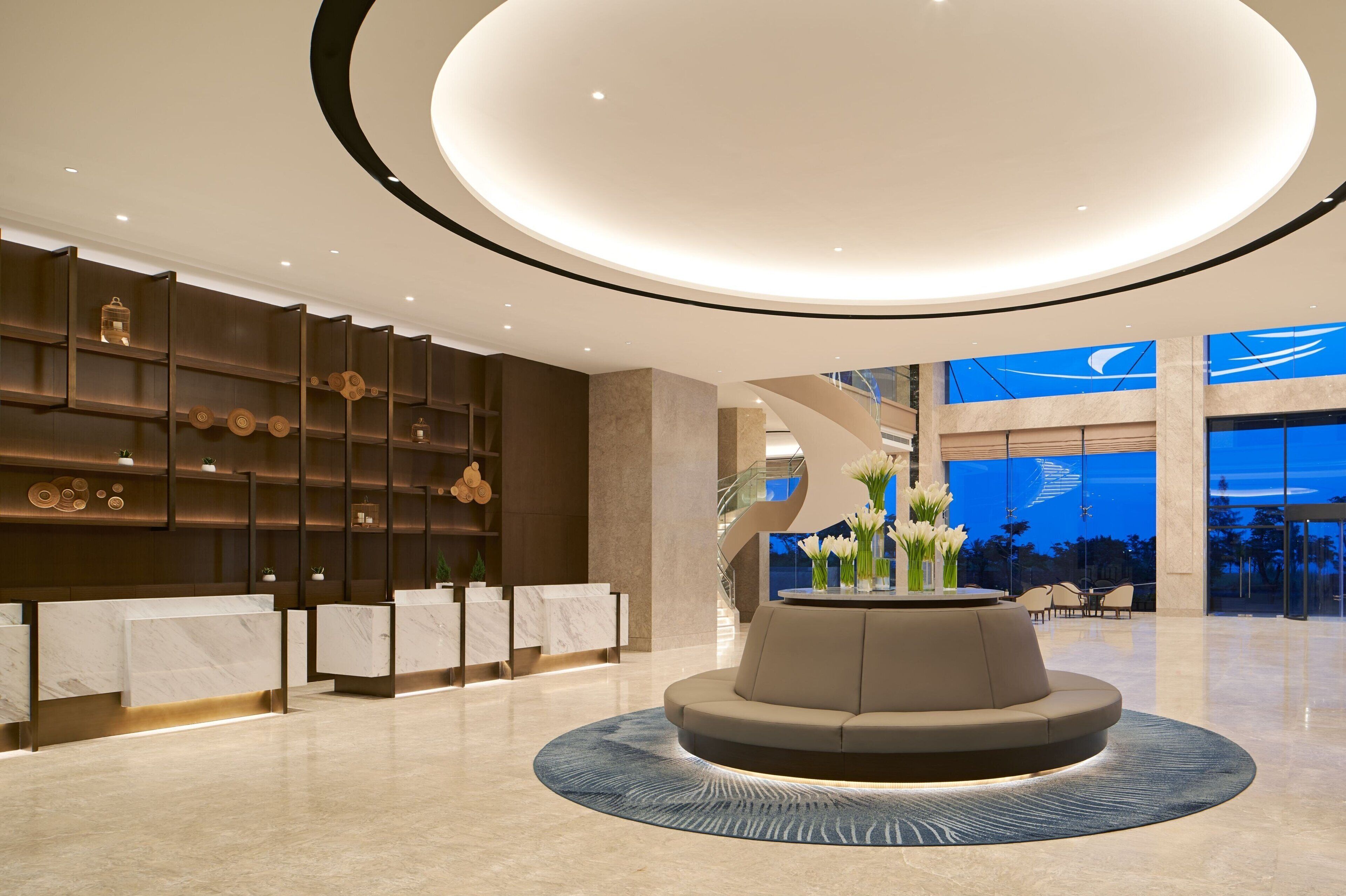 A modern lobby with a central seating area, marble reception desks, and a large window with a view of the sky.