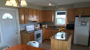 A kitchen with wooden cabinets, a white stove, a refrigerator, and a dining table with chairs. - Oysterbay Cottage - Fun, Beach and Food!!! License number 2100974 (Darnley)