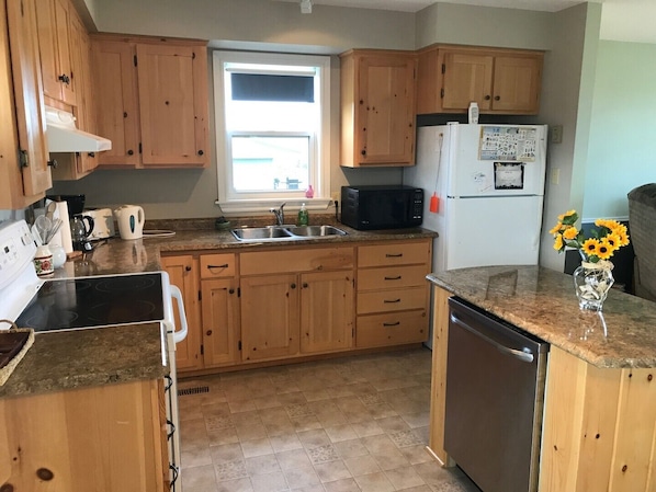 A kitchen with wooden cabinets, a microwave, a refrigerator, and a window.