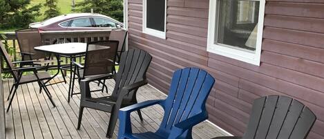 Une terrasse en bois avec des fauteuils Adirondack et une table, donnant sur un quartier résidentiel.