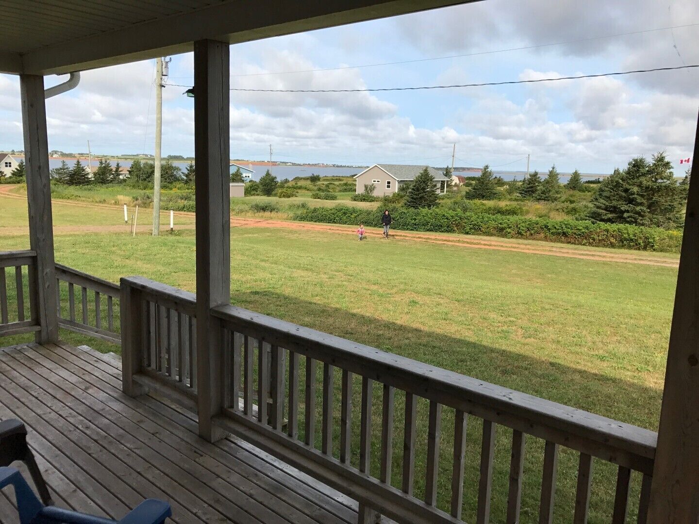A wooden deck with a view of a grassy field and a body of water in the distance.