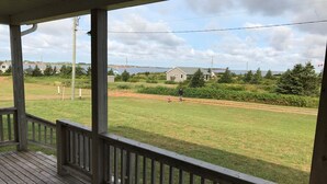 A wooden deck with a view of a grassy field and a body of water in the distance. - Oysterbay Cottage - Fun, Beach and Food!!! License number 2100974 (Darnley)
