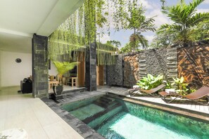 A modern indoor pool area with a stone wall, hanging plants, and lounge chairs. - Puri Bagus Villa Legian Kuta (Kuta)