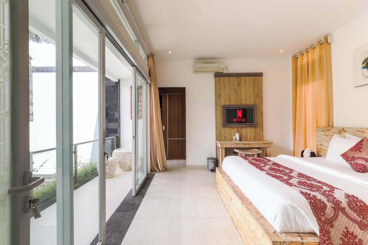 Una habitación de hotel moderna con una cama grande, un televisor montado en la pared y una puerta corredera de vidrio que da a un espacio exterior.