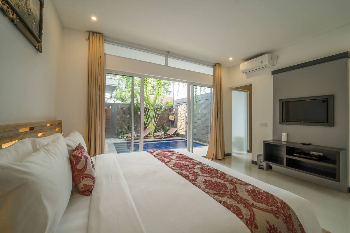 Una habitación de hotel moderna con una cama grande, un televisor y vista a una piscina.