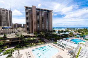A high-rise hotel with a rooftop pool, palm trees, and a view of the ocean.