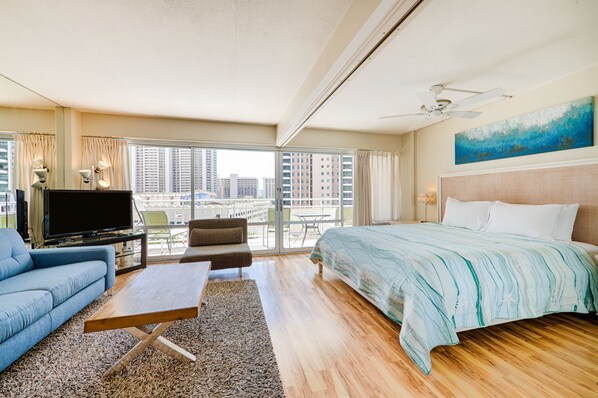 A modern hotel room with a large bed, a sofa, a TV, and a balcony with a city view.