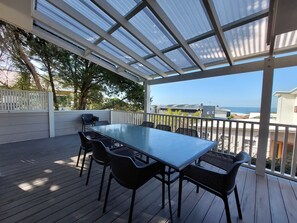 Un patio techado al aire libre con una mesa y sillas, con vistas a una zona residencial y al mar.